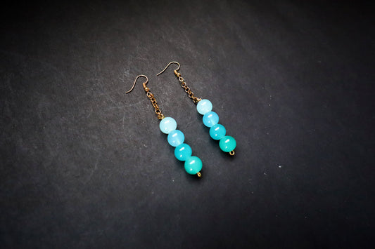 Angled view of Pair of Turquoise handcrafted Gradient Glass Bead & Golden Chain Dangle Earrings on black fabric background