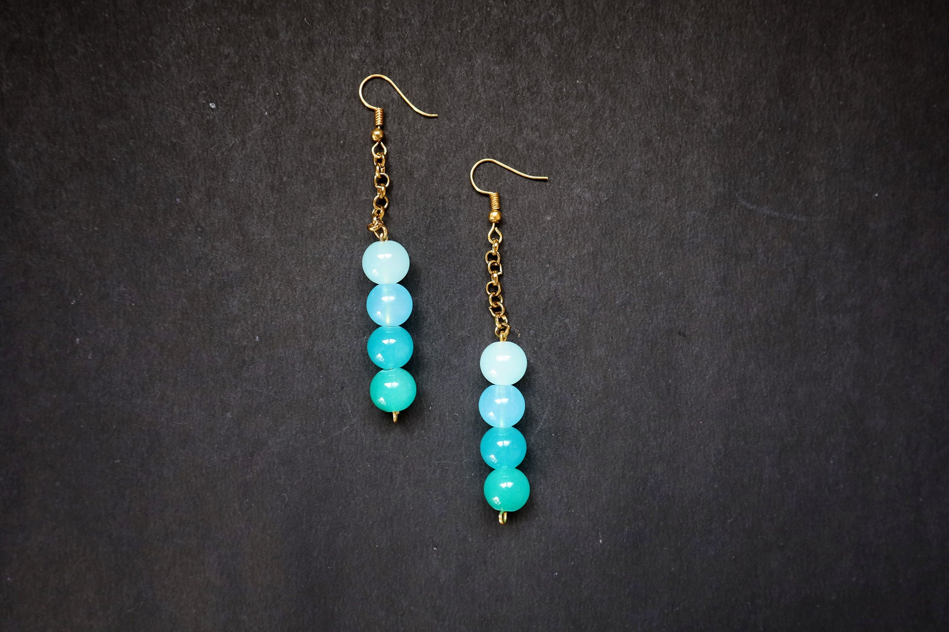 Close-up of Pair of Turquoise Gradient Glass Bead & Golden Chain Dangle Earrings on black jewellery mannequin