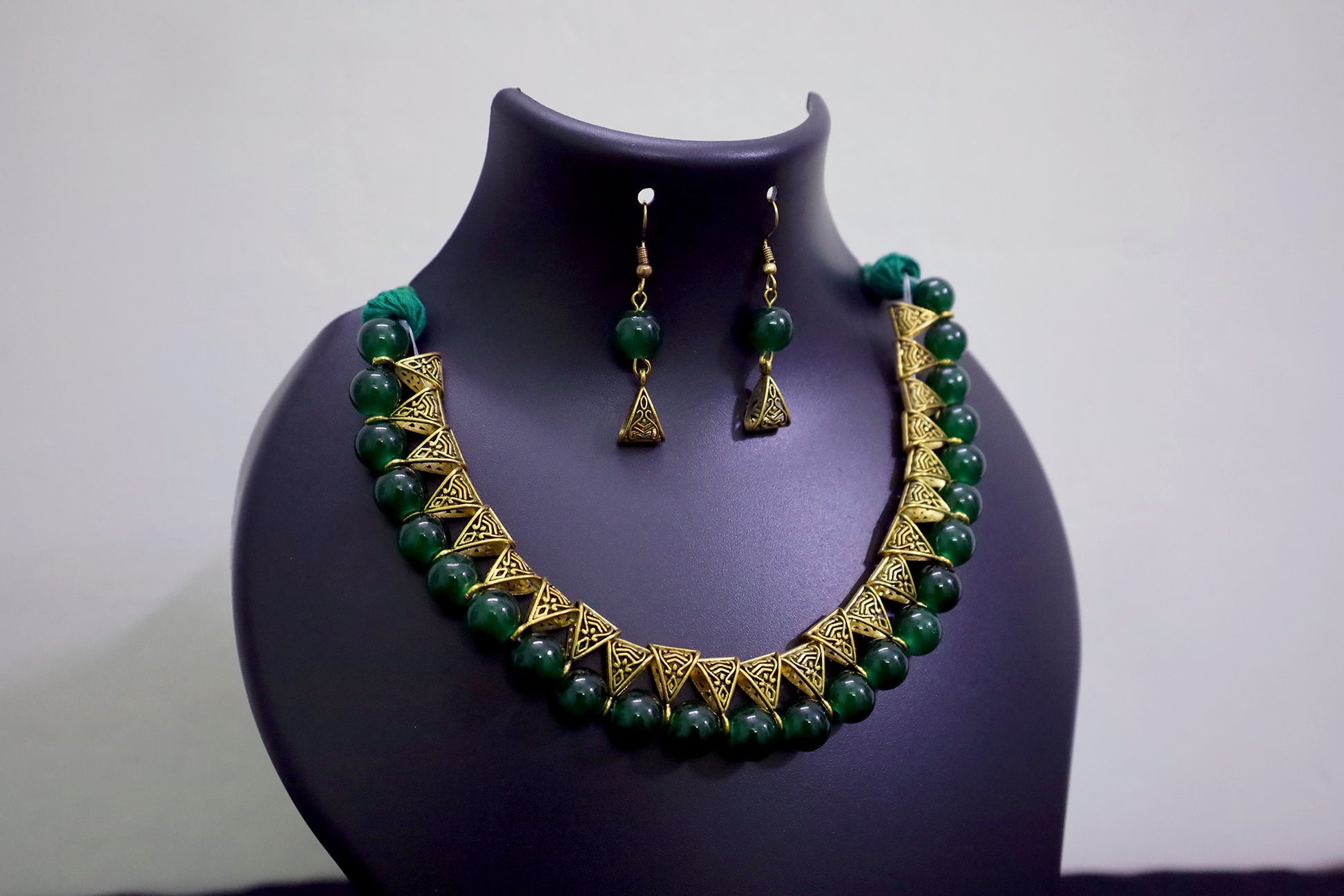 Closer view of green glass beads golden loop necklace set on black mannequin