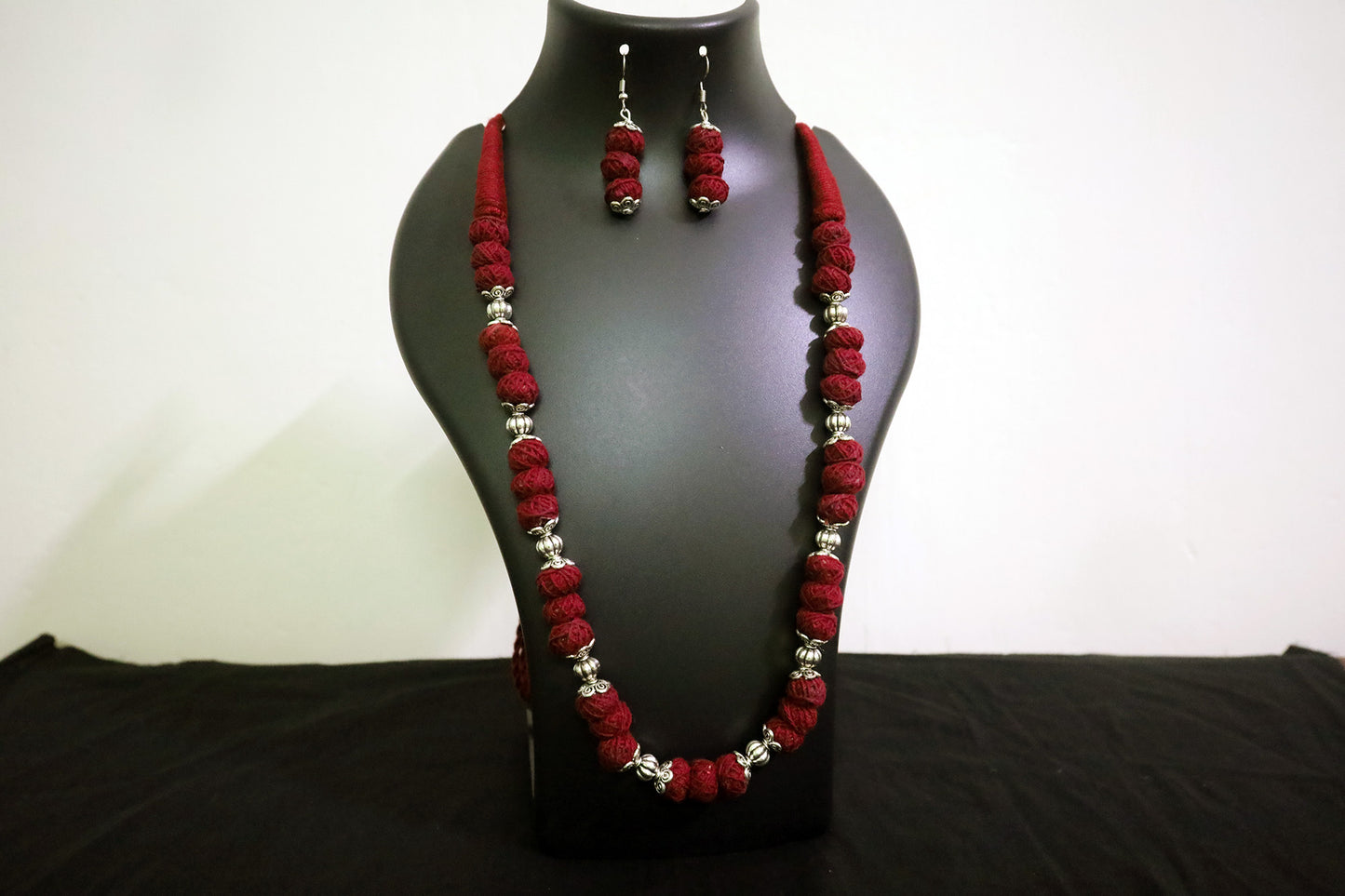 Closer view of maroon oxidized and cotton balls long necklace with earrings on black mannequin.