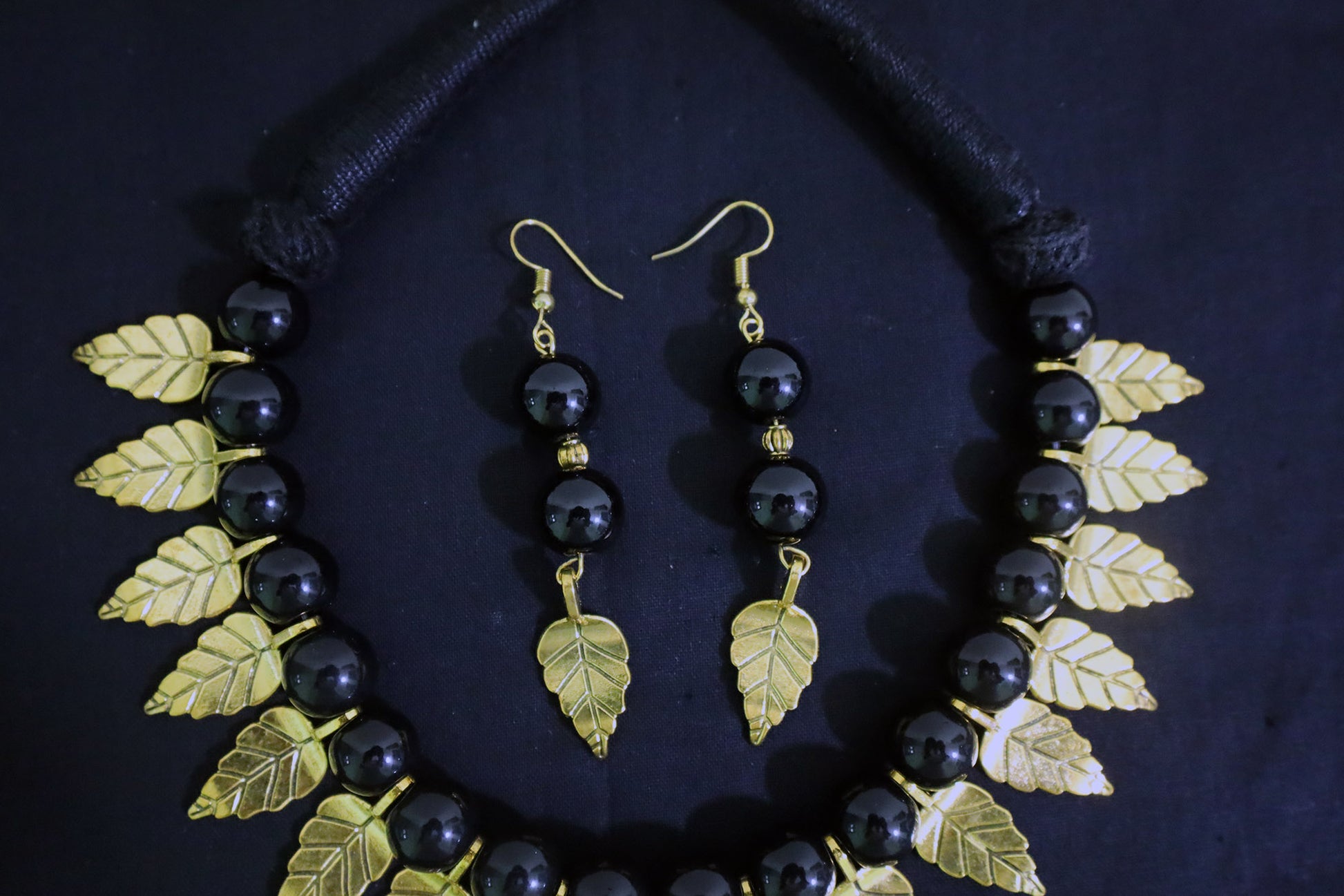 Middle section close view showing black glass beads and golden leaf charm detailing of the handmade necklace.