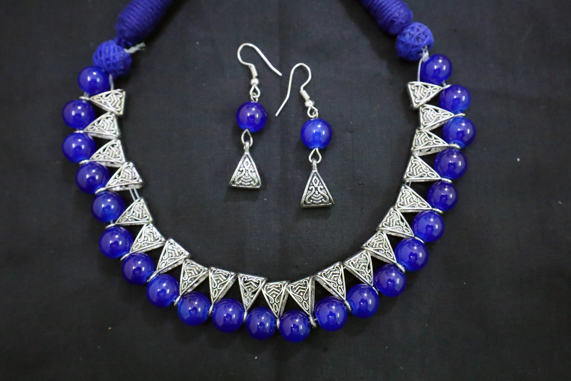 Bottom close-up of navy blue glass beads silver loop necklace and earrings