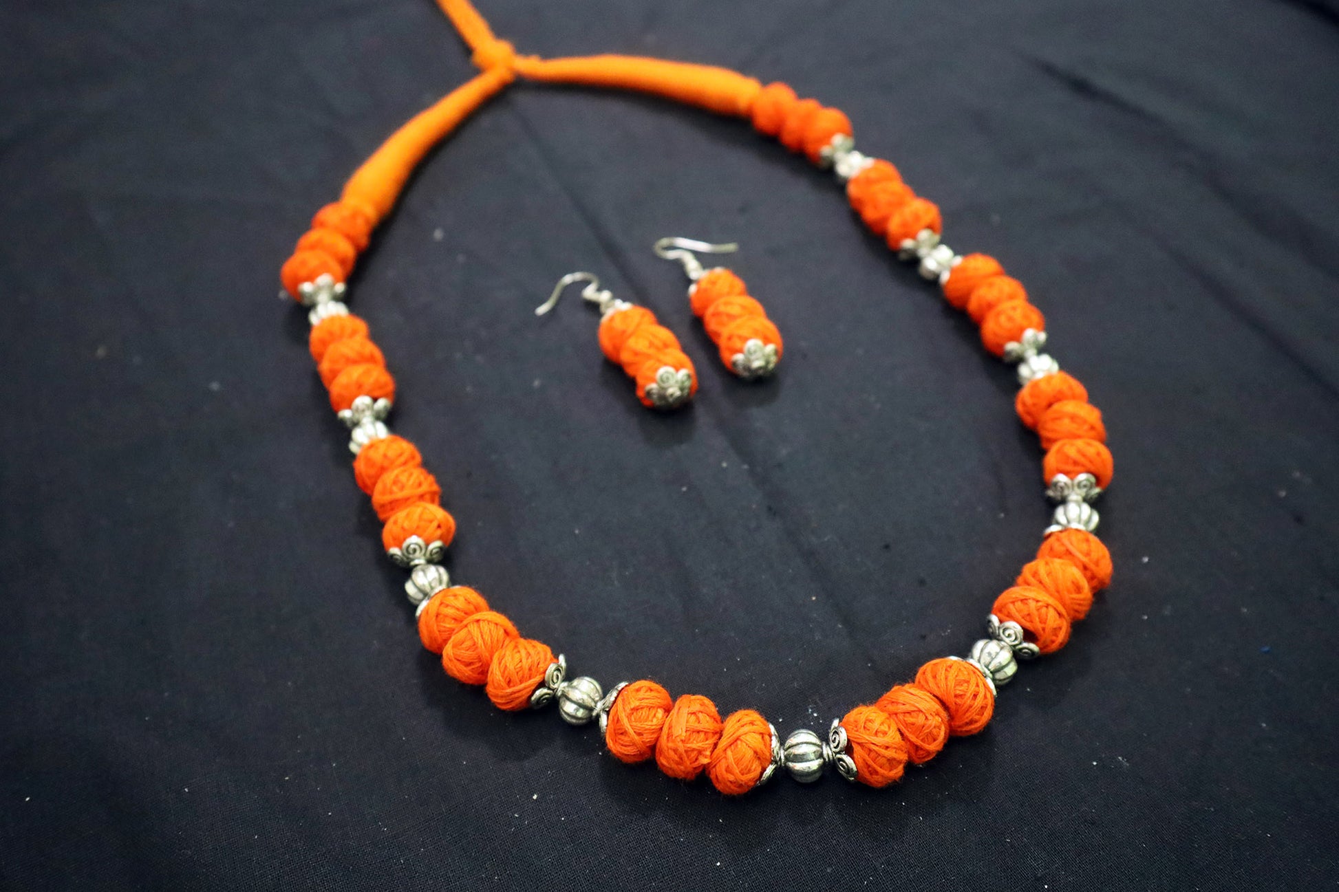 Angle view of orange oxidized balls and cotton balls necklace with earrings