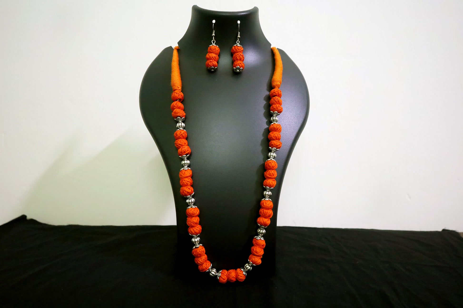 Closer view of orange oxidized balls and cotton balls long necklace with earrings on black mannequin