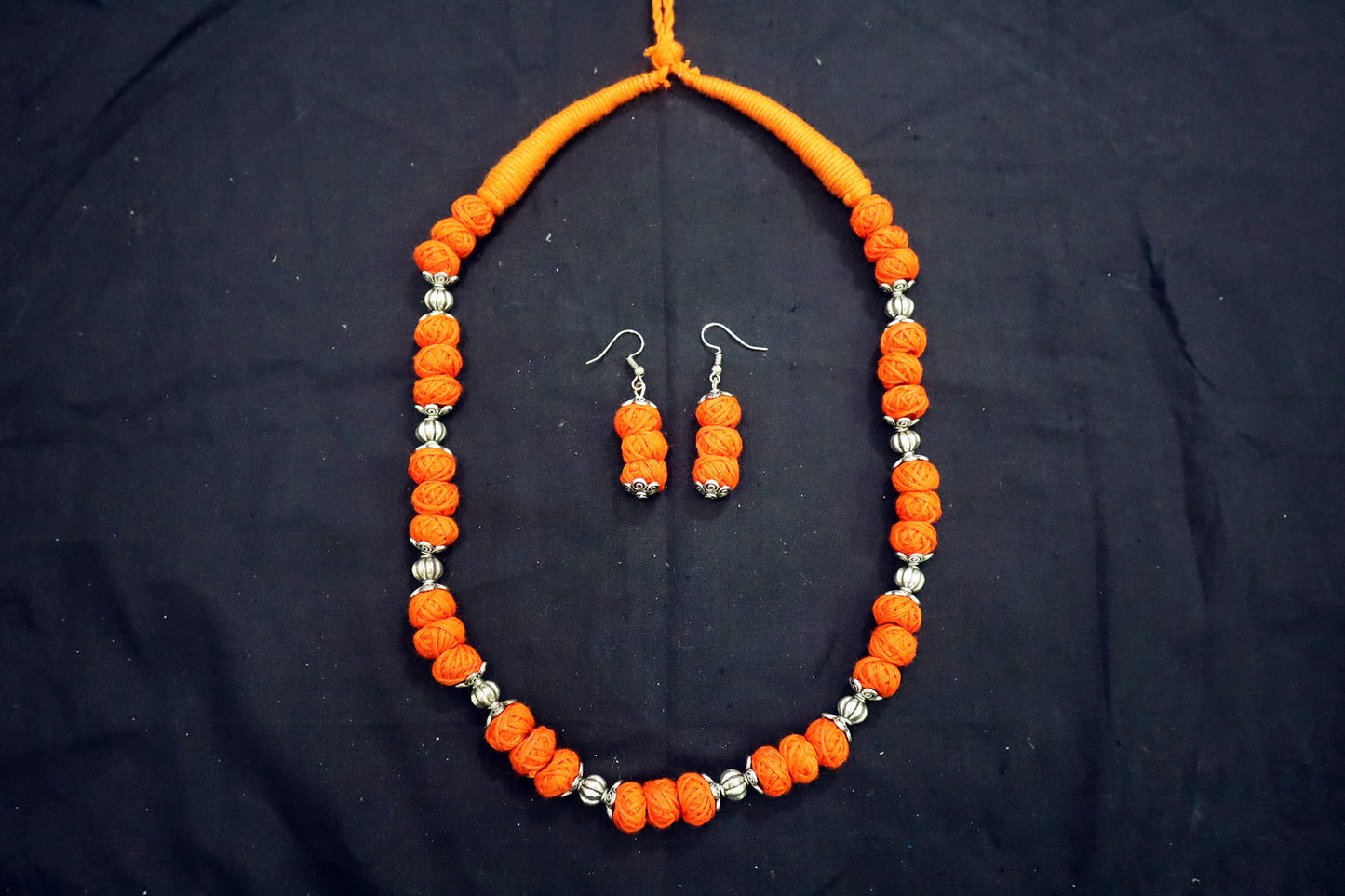 Top view of orange oxidized and cotton balls long necklace set on black background