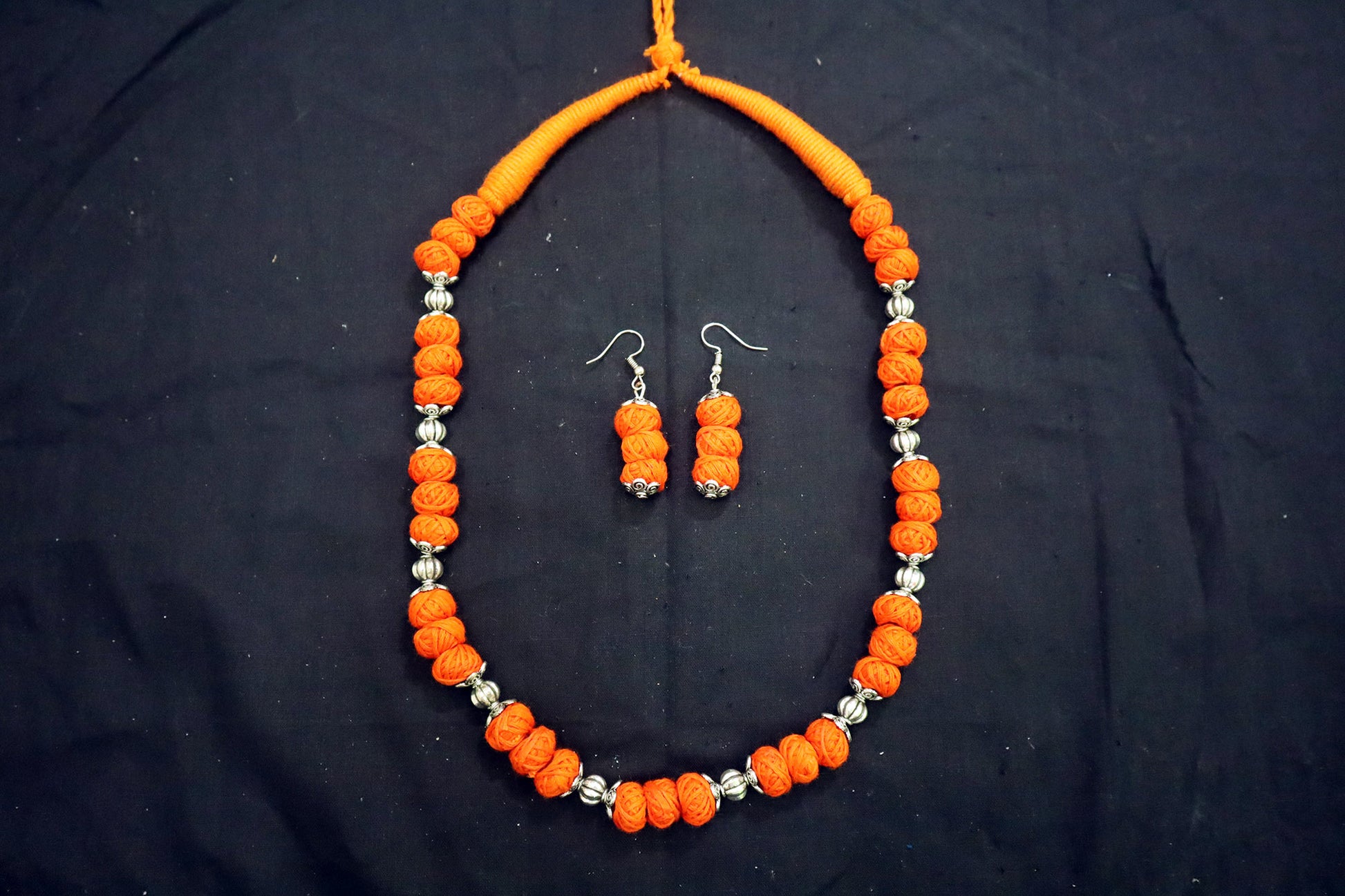 Top view of orange oxidized and cotton balls long necklace set on black background