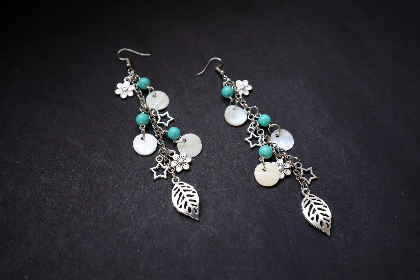 Angle view of oxidized long chain earrings with pearl, turquoise beads, and multiple charms