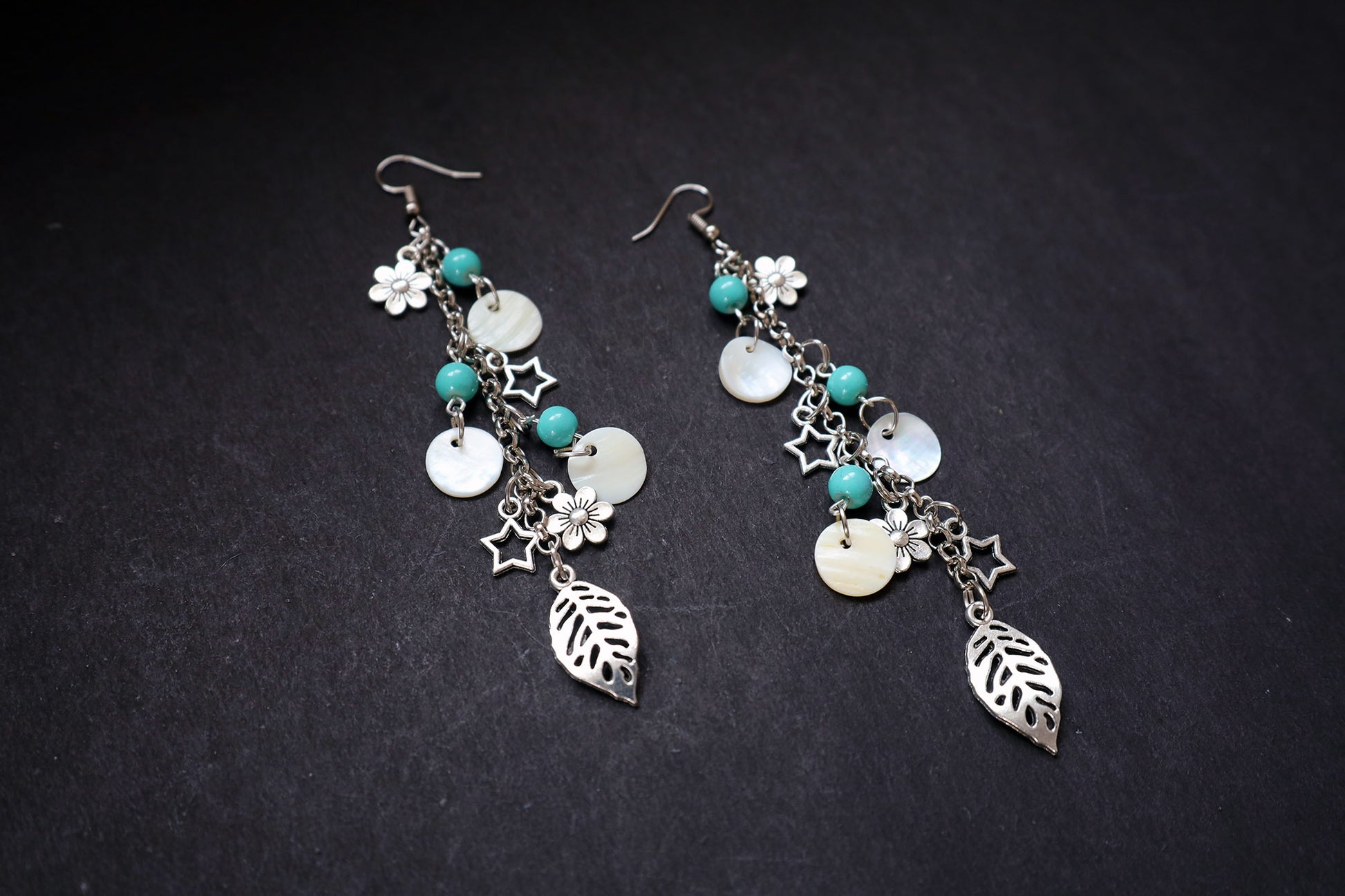 Angle view of oxidized long chain earrings with pearl, turquoise beads, and multiple charms