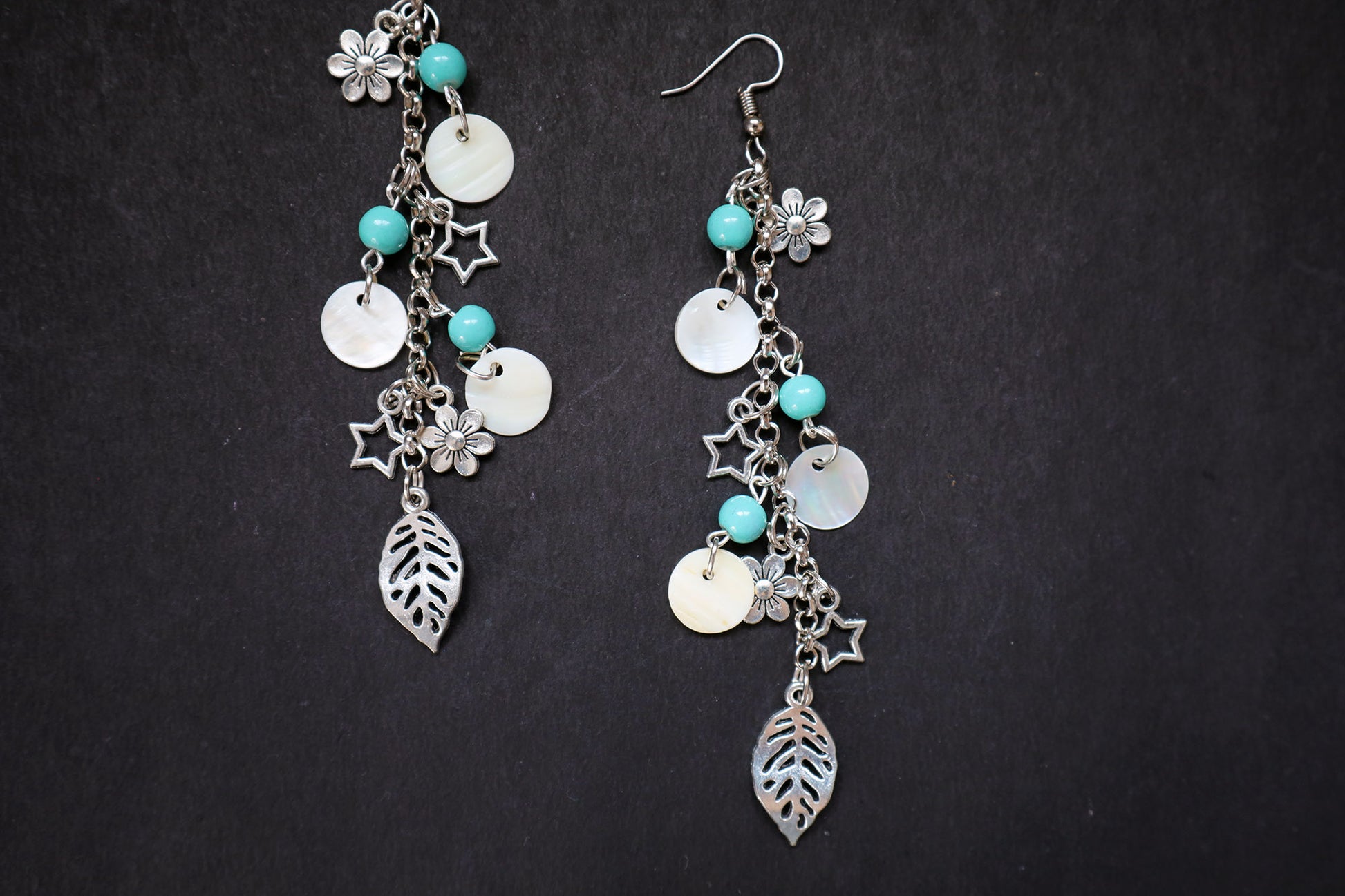 Closer view of pair of silver earrings with turquoise beads and leaf charms on a black background