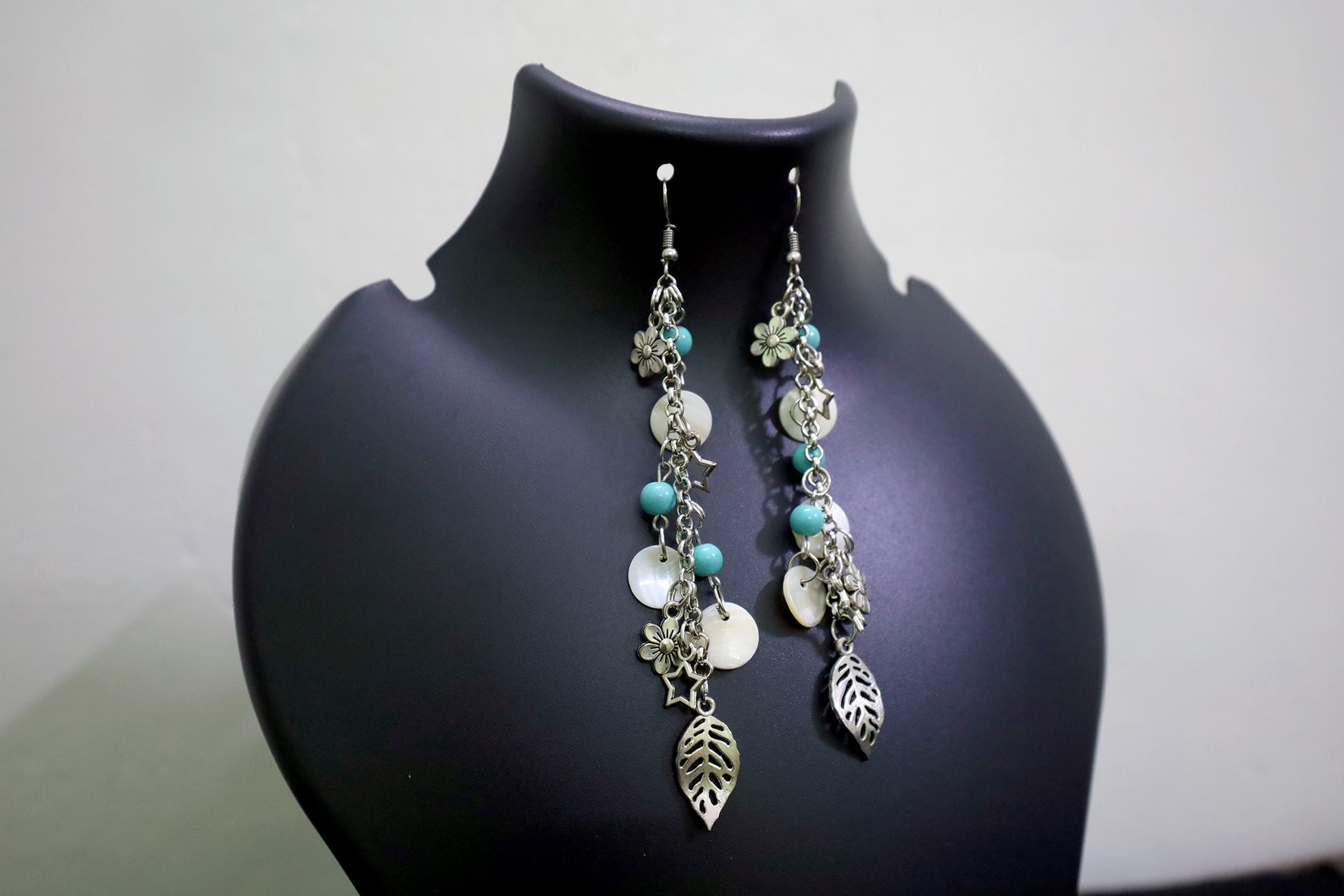 Closer view of pearl and oxidized long chain earrings with charms on black jewellery mannequin