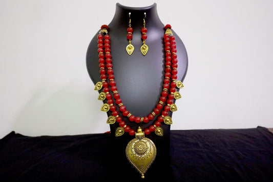 Closer look of red glass beads and golden drop pendant necklace with earrings on black mannequin.