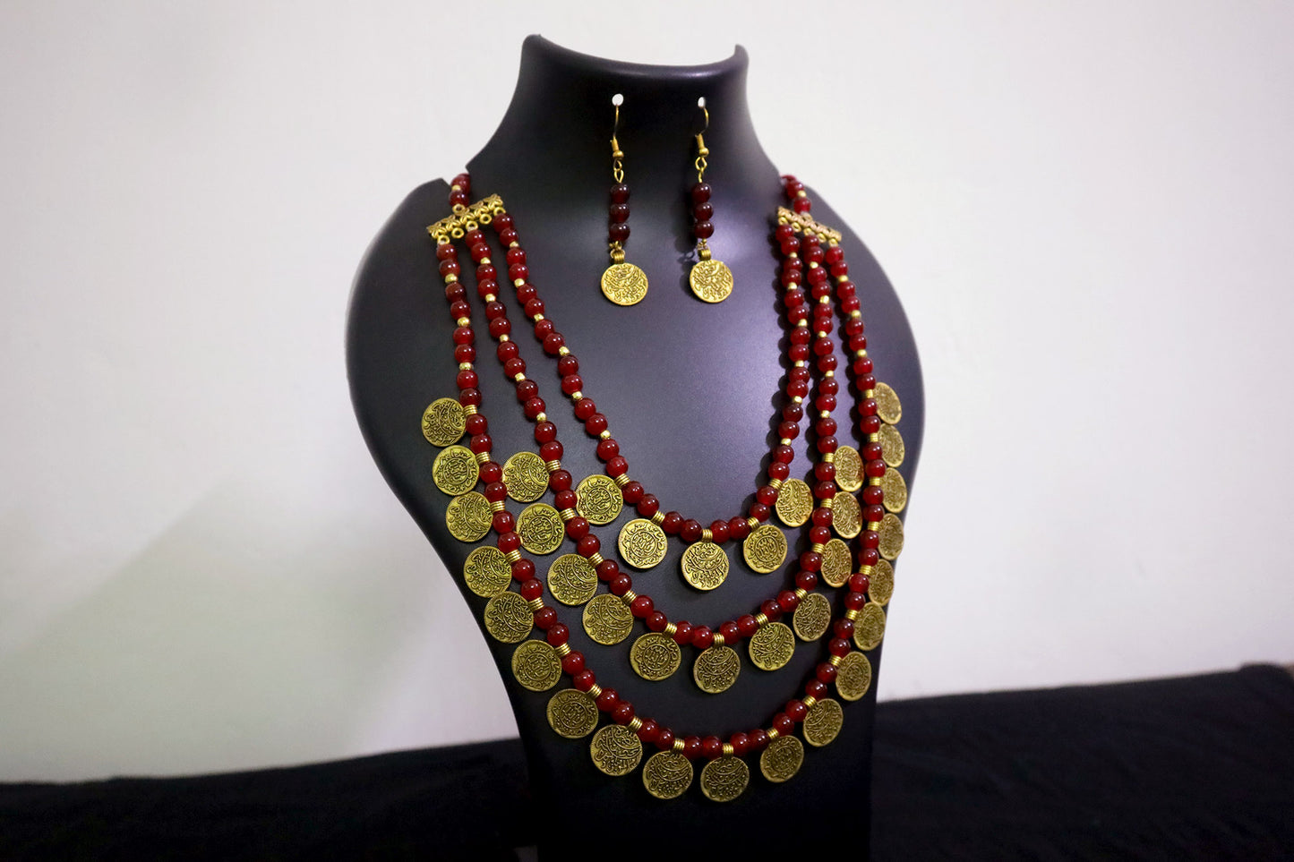 Closer view of 3 layered glass beads and golden ginni necklace with earrings on black jewellery mannequin