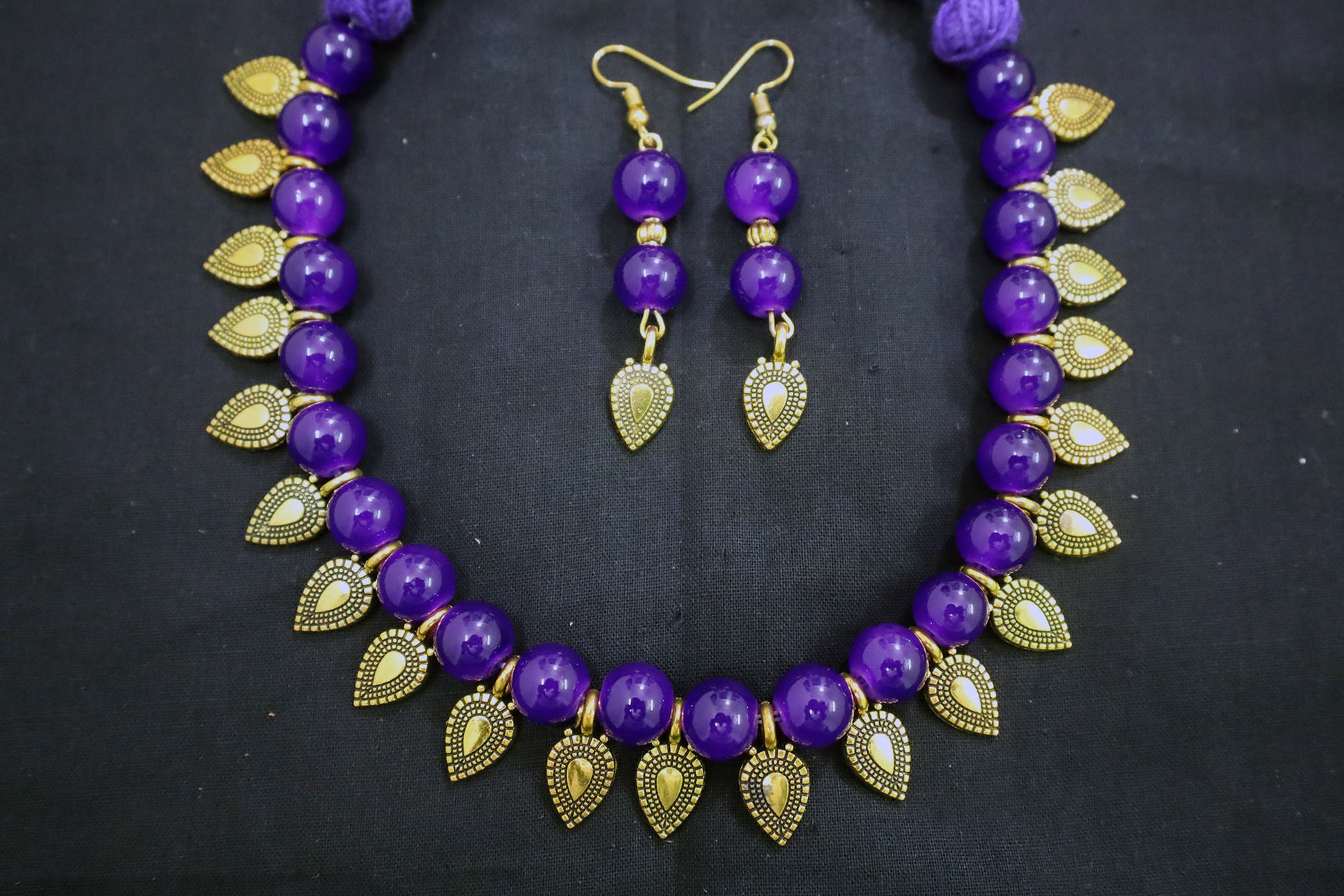 Violet beaded necklace with gold leaf and earrings on a black background - fashion jewellery online
