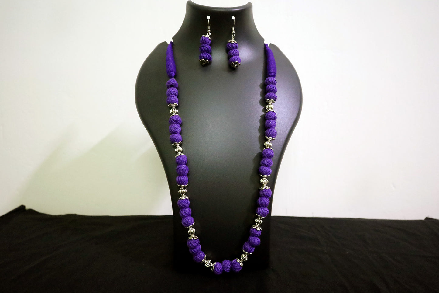 Closer view of violet oxidized and cotton balls long necklace with earrings on black mannequin.